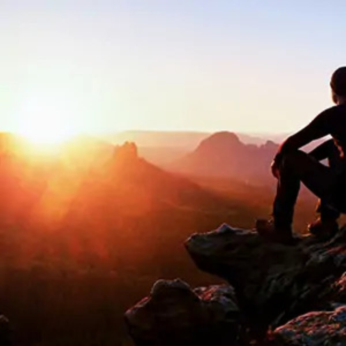 Climber resting on rocks looking out at sunrise