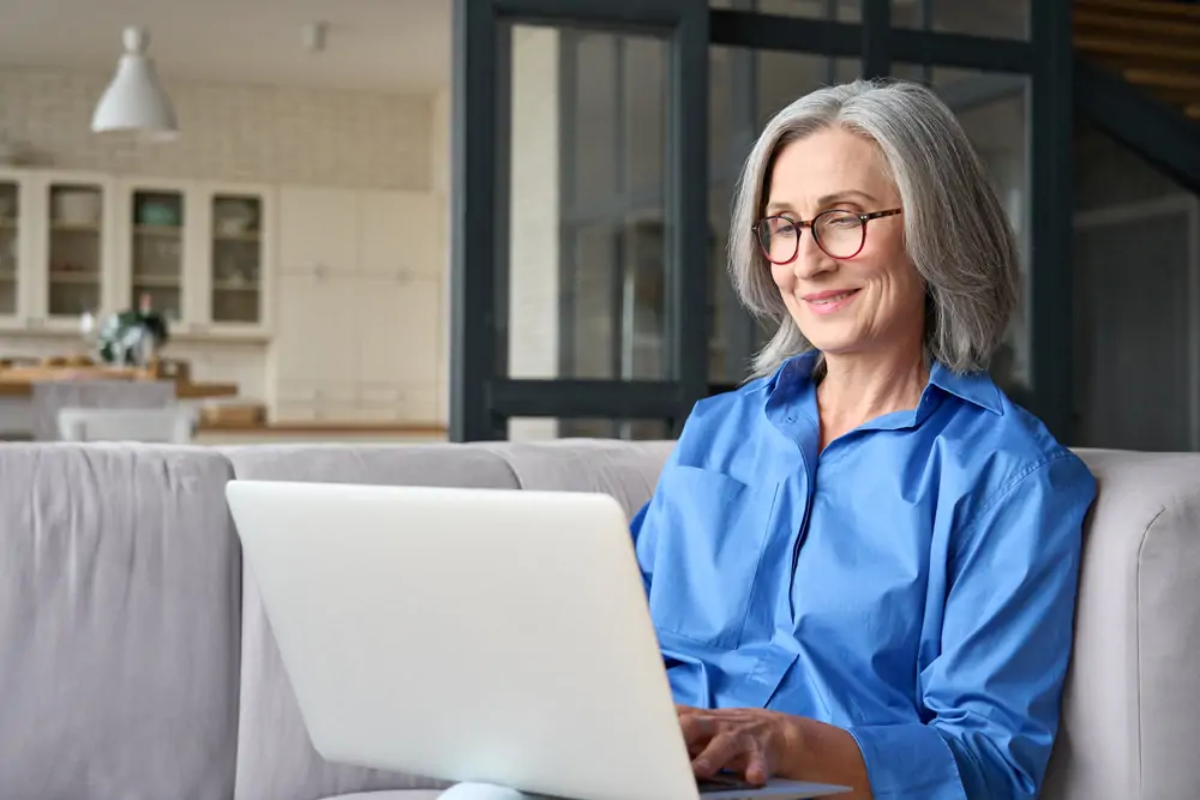 Elderly woman sitting on sofa using laptop to file Self Assessment tax return
