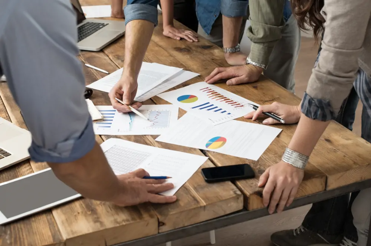 Businesspeople standing around table lookin at printed business performance graphs