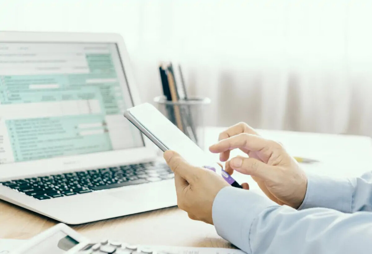 Businessman using smartphone at desk in front of open laptop