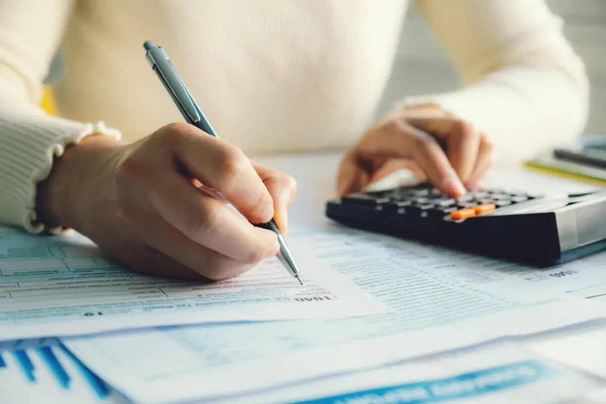 Businesswoman using calculator in one hand and filling in tax form with pen with the other