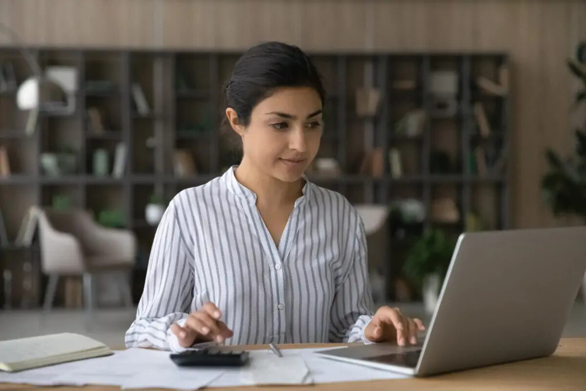 Businesswoman using calculator with one hand and laptop with the other to calculate corporation tax