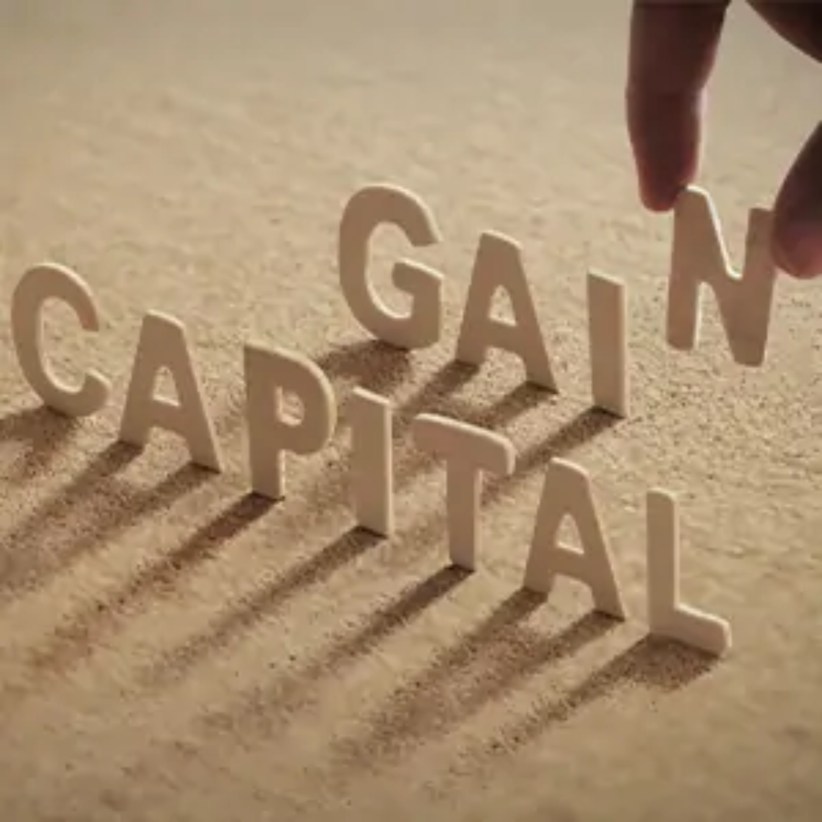 Hand placing paper letters upright on surface spelling out 'Capital Gains'