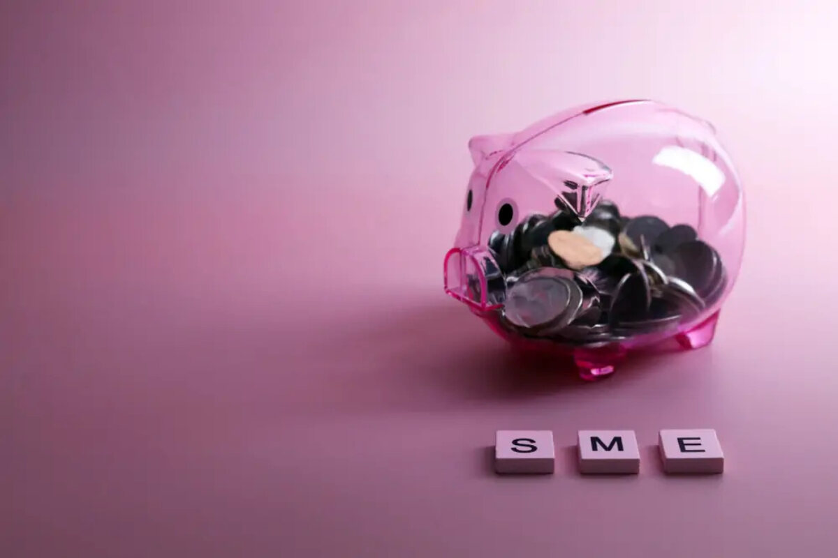 Transparent piggy bank half-filled with coins, with three tiles spelling out 'SME' in front