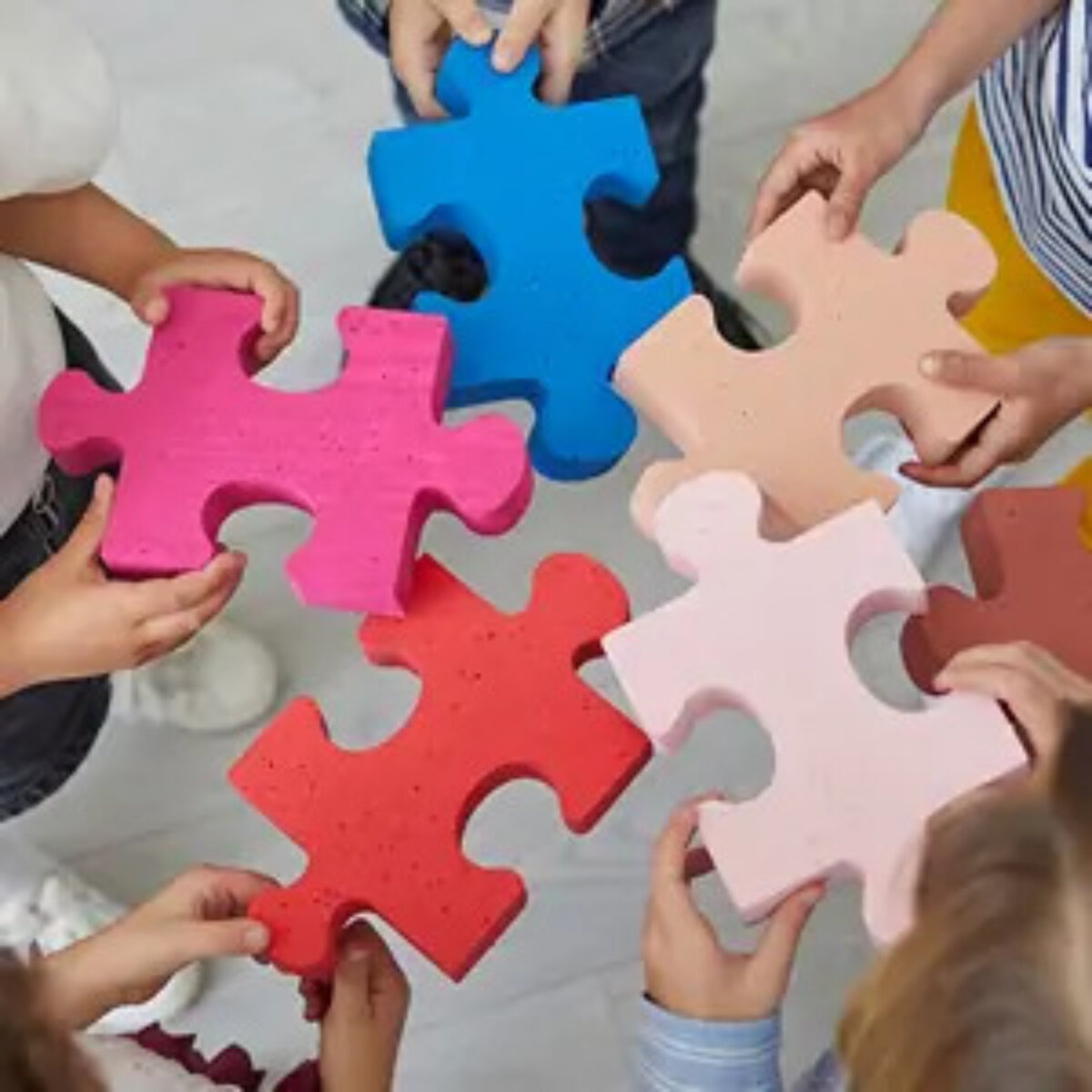 Five people standing in circle each holding a giant jigsaw piece in the middle