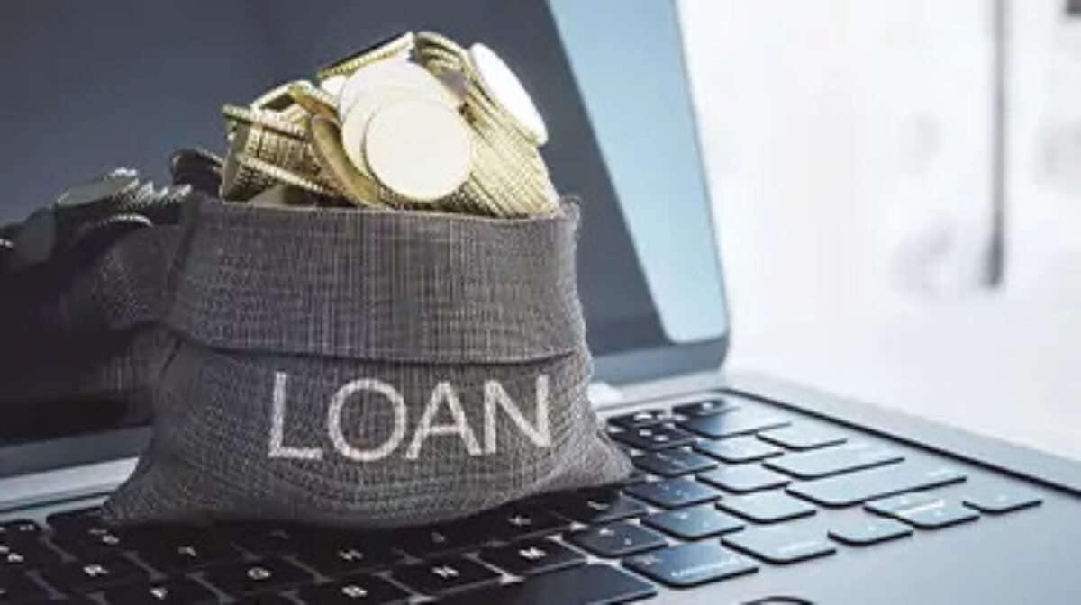Small sack with 'loan' written on the front filled with gold coins, sitting on top of a laptop keyboard