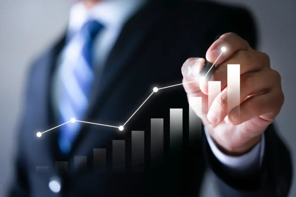 Businessman holding pen at plot point of image of an increasing line graph above an increasing bar chart
