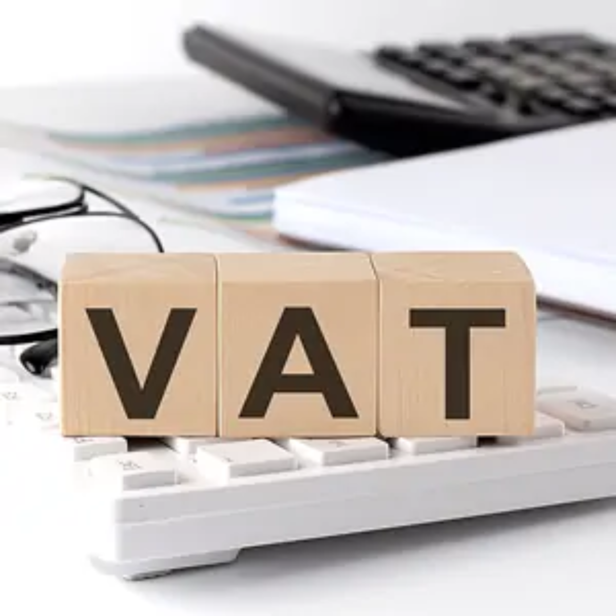 Wooden blocks with letters on them arranged on top of a calculator to spell out VAT