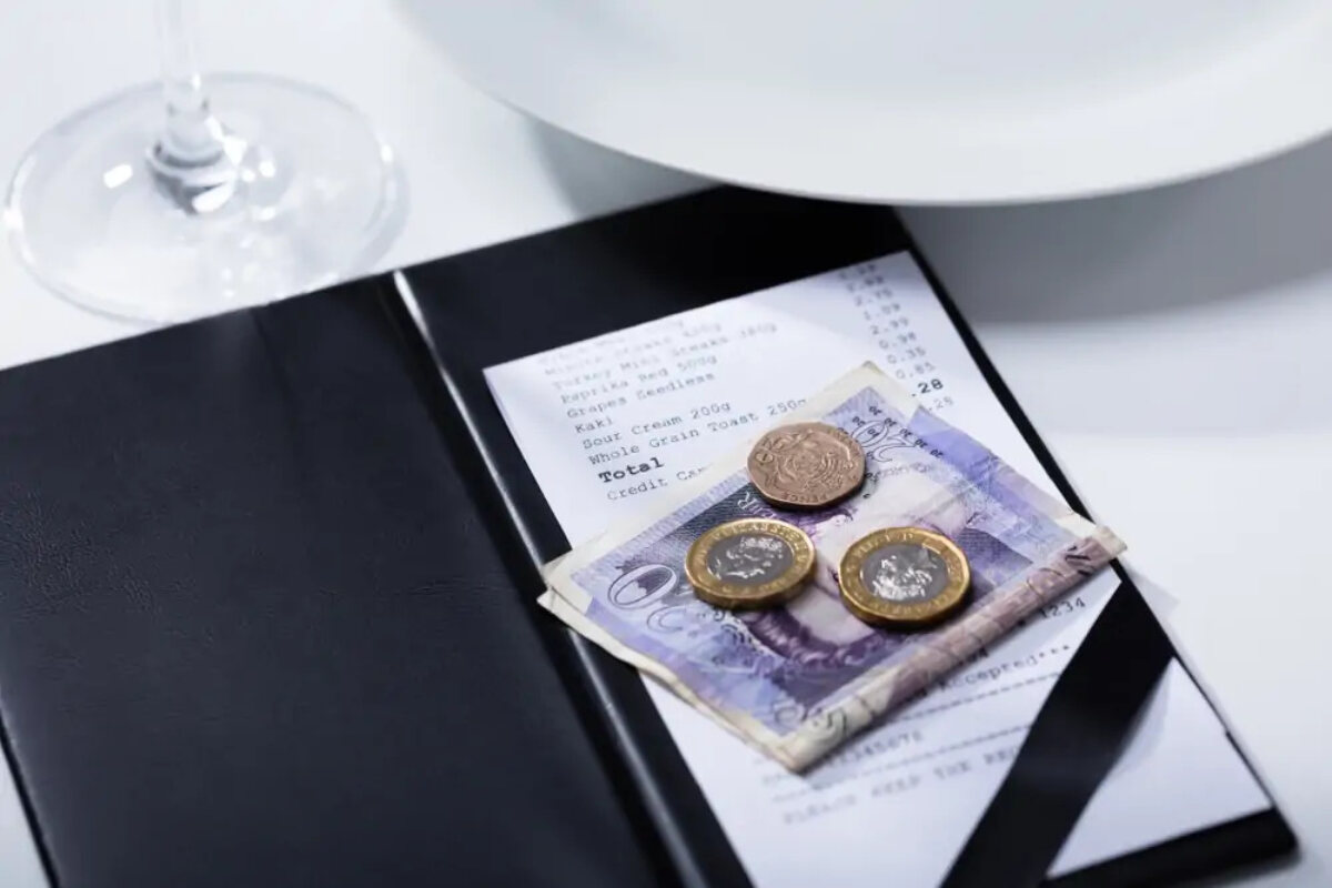 twenty pound note and three coins on top of a restaurant bill on table