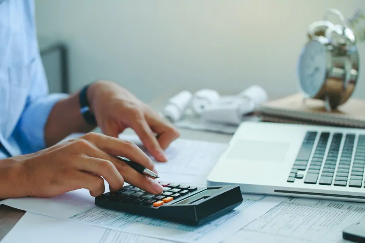 Businessperson at desk using calculator with one hand and pointing at tax return document with the other