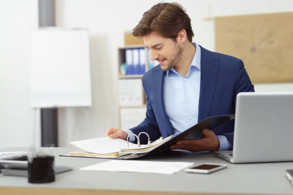 Businessman at desk looking at tax records in ring binder