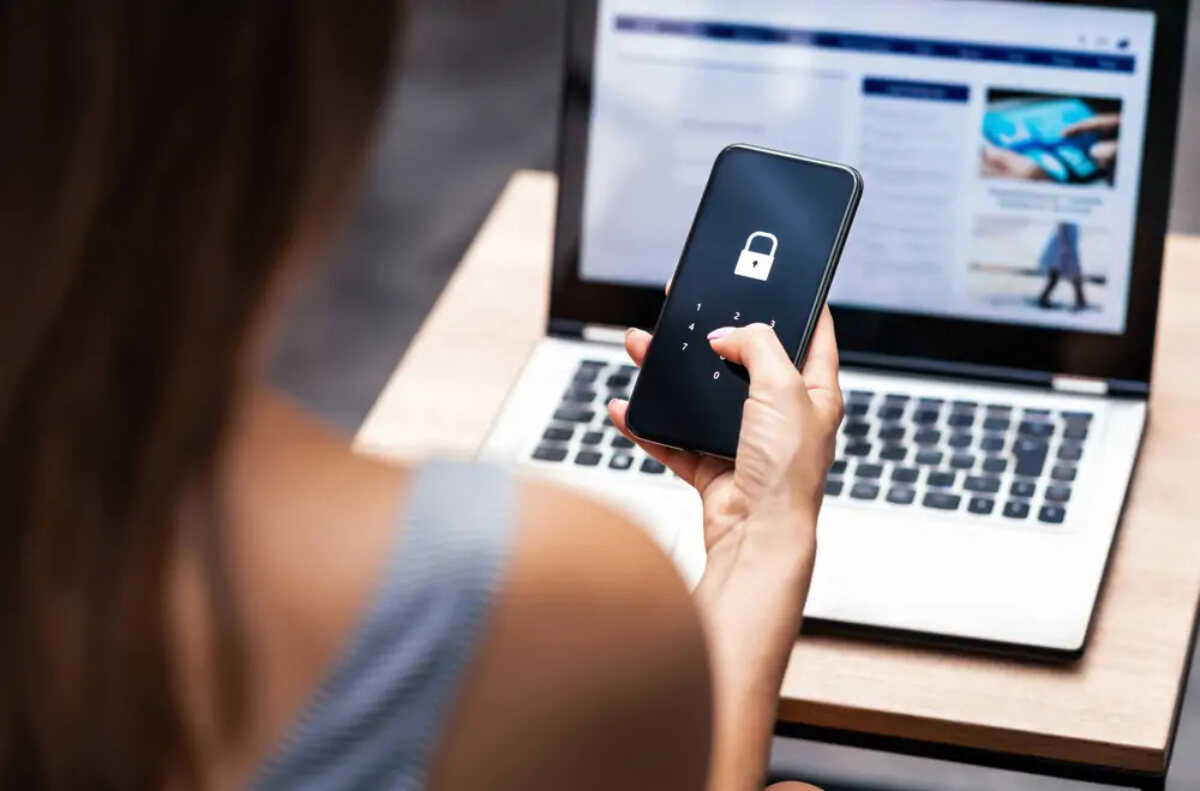 Woman entering passcode to unlock smartphone in front of open laptop