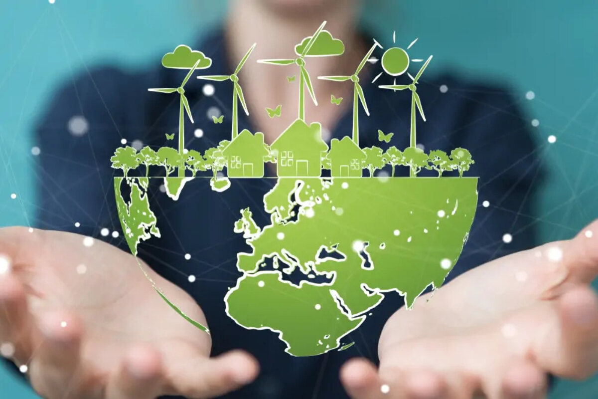 Hands holding globe-shaped image with map of the world on bottom half and houses, trees, wind turbines and sky on top half