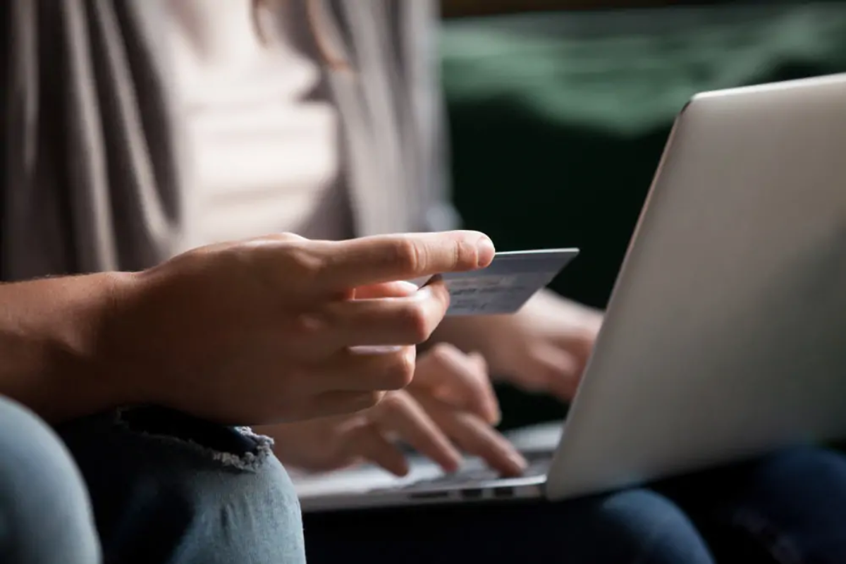 Man sitting down with bank card in hand in front of woman sitting with laptop