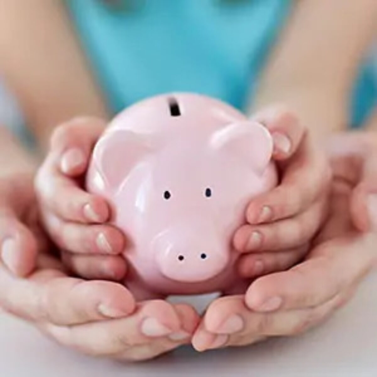 Adult's hands cupping child's hands holding piggy bank