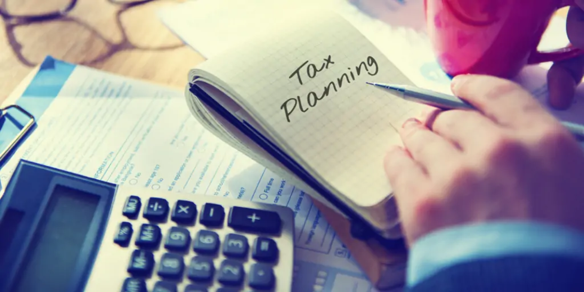 Hand holding pen over open notebook with 'tax planning' written on page