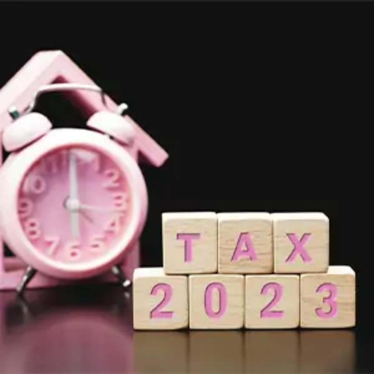 Wooden blocks with letters on them arranged to spell out 'tax 2023' in front of wooden house silhouette and alarm clock