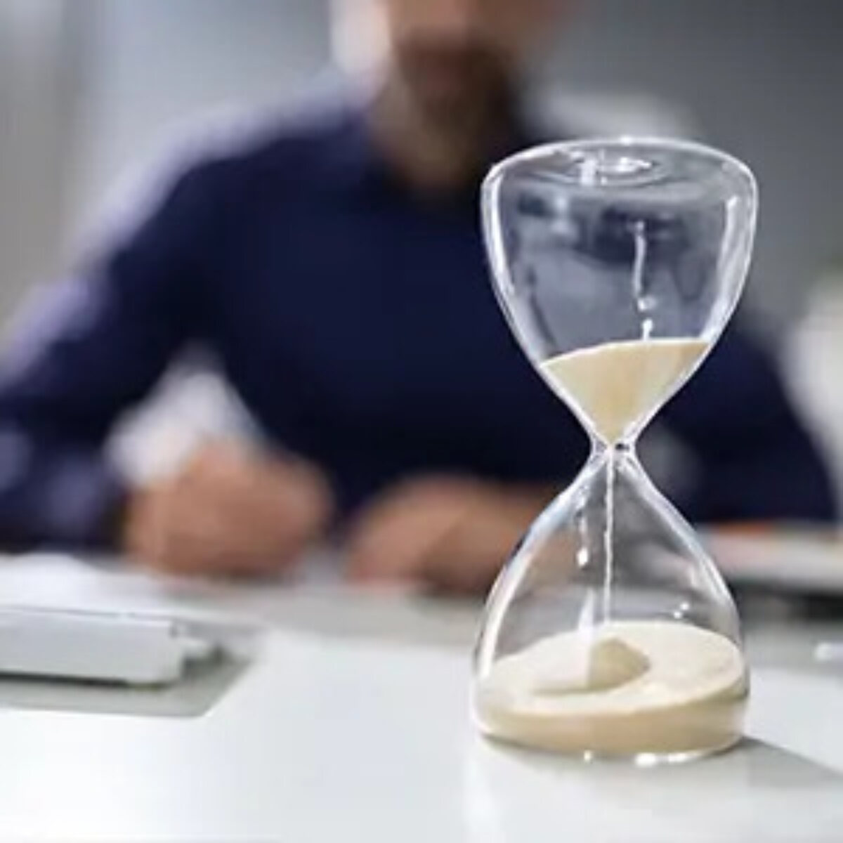 Sand timer in progress on desk with out-of-focus businessman in background