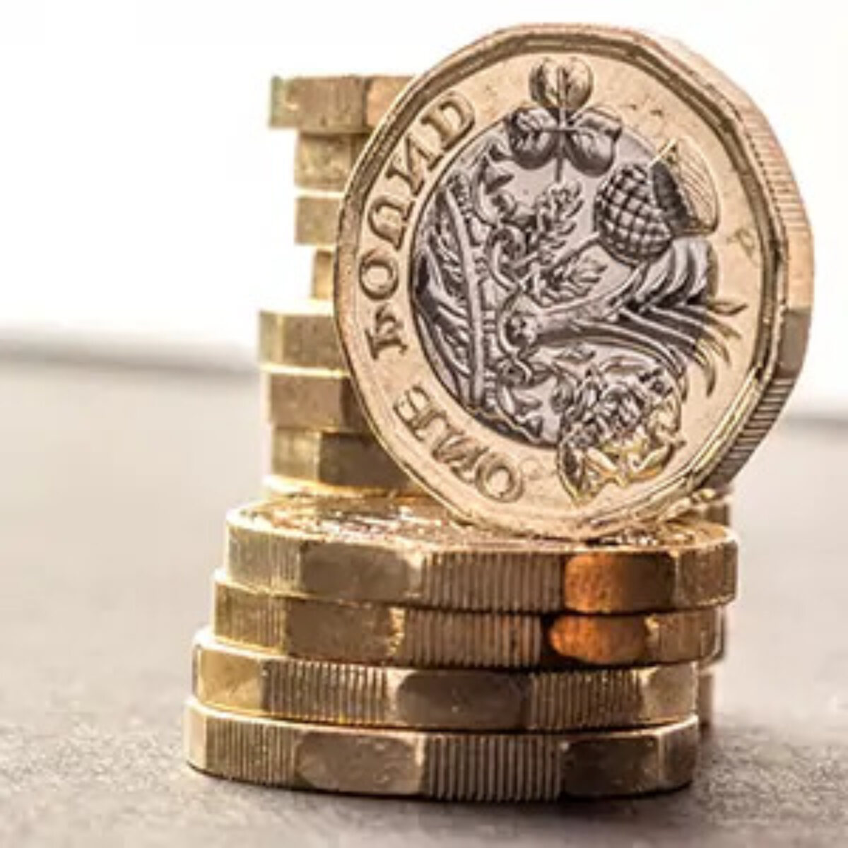 A taller stack of pound coins behind a shorter stack with an upright pound coin balanced on top