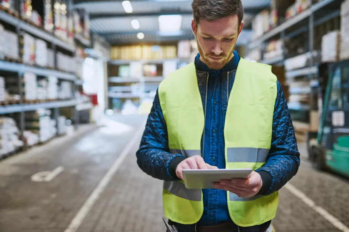 Warehouse worker in high-vis standing using tablet