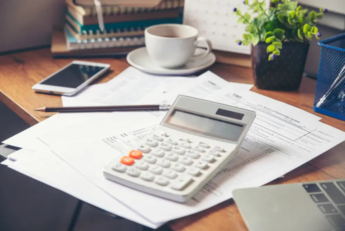 Calculator on desk on top of documents next to pencil, smartphone and cup of coffee