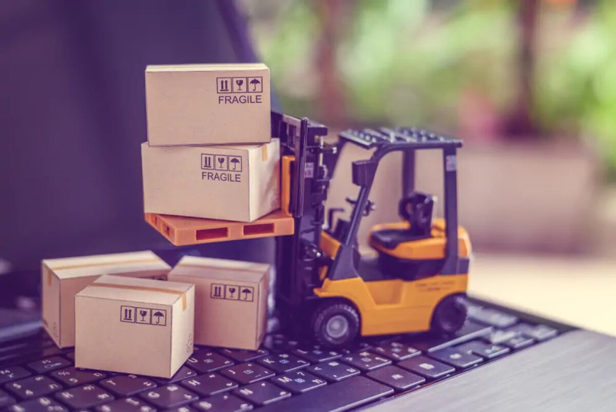 Toy forklift truck lifting miniature cardboard boxes on top of laptop keyboard