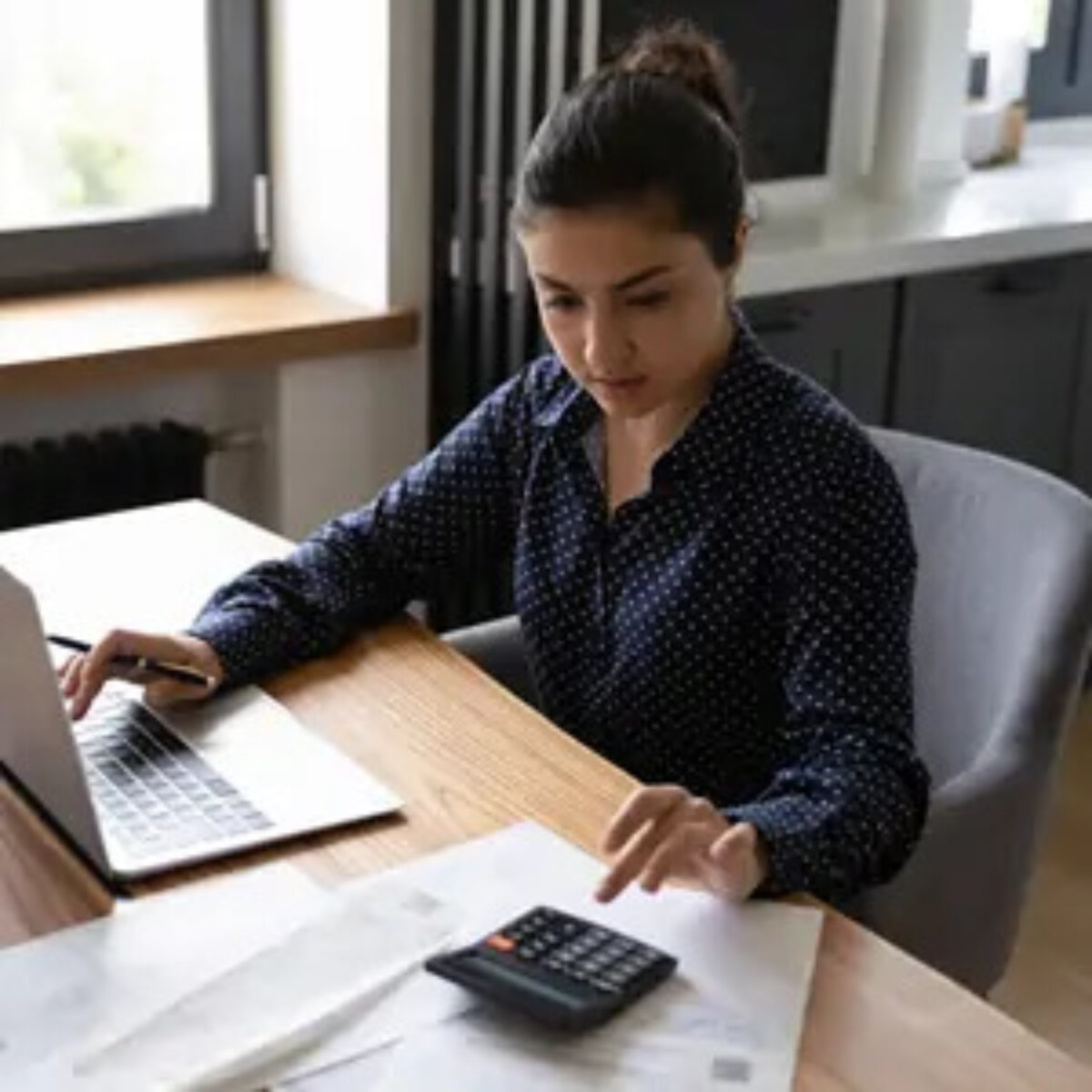 Businesswoman using calculator with one hand and laptop with the other