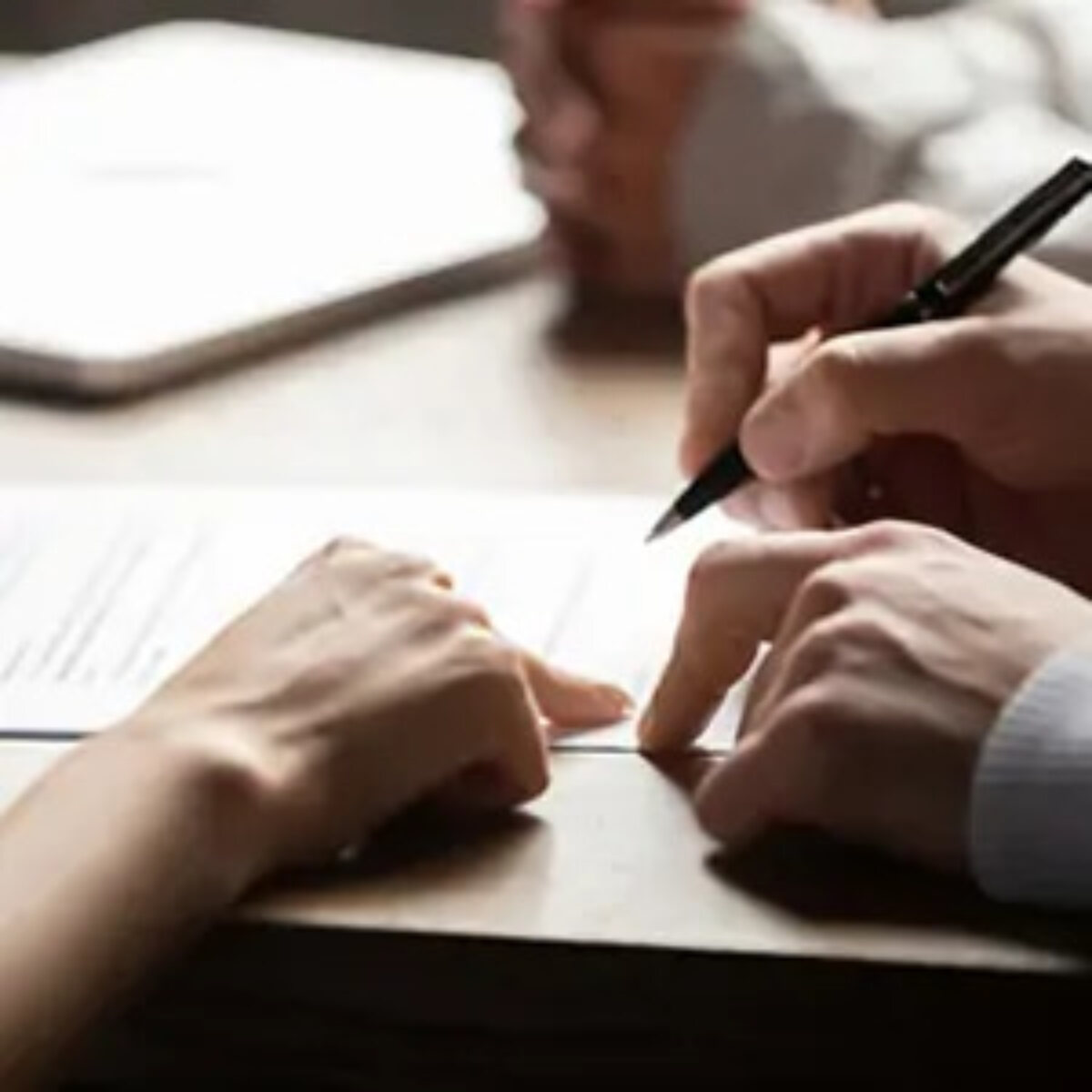 Two hands pointing at document on table and one hand holding a pen over it