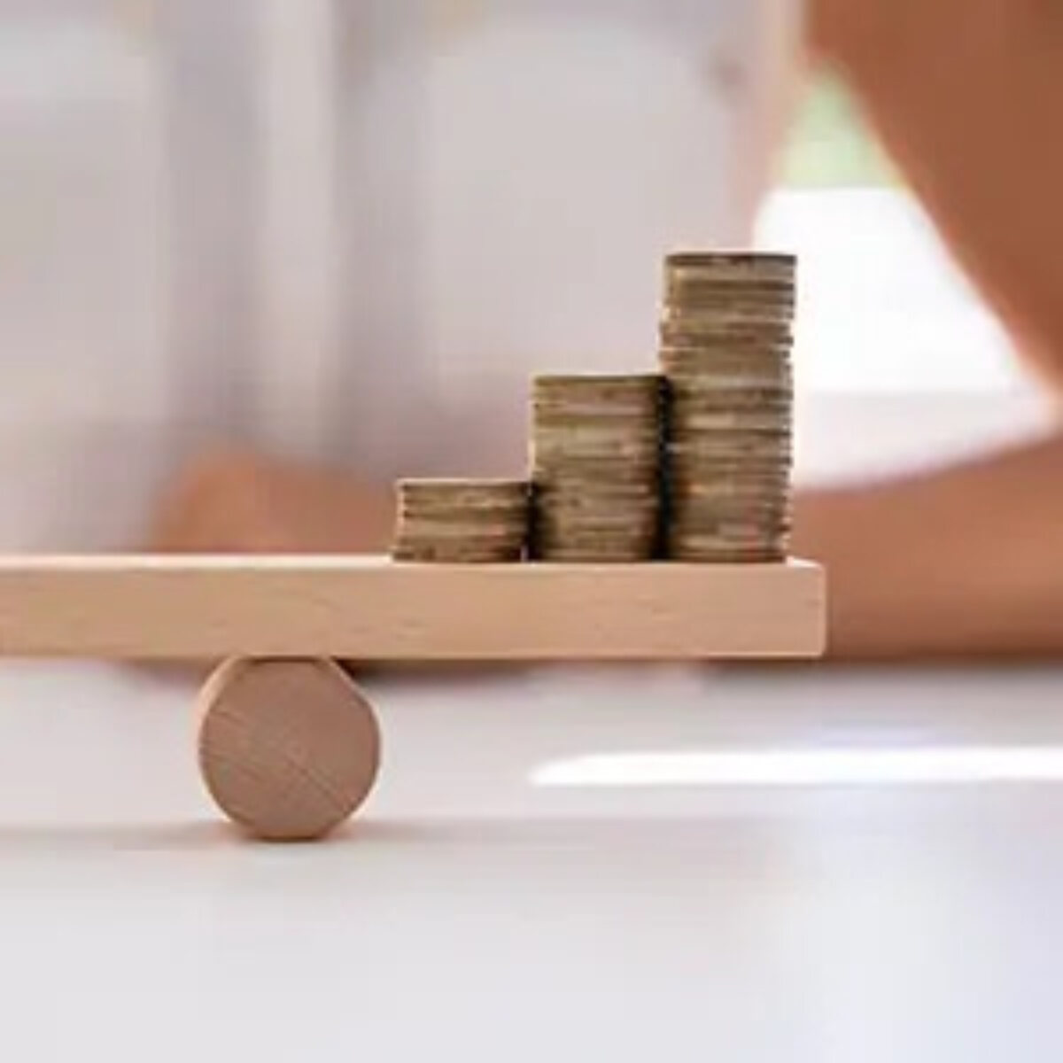 Three stacks of coins sitting on one side of a balanced miniature wooden seesaw