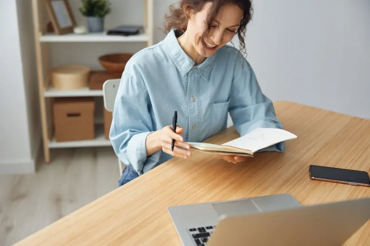 Businesswoman sitting at desk holding and smiling at open notebook