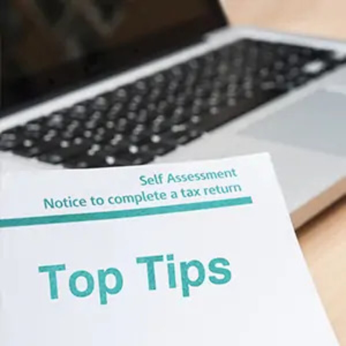 Sheet of paper with 'Self Assessment notice to complete a tax return' header and 'top tips' beneath, in front of an open laptop