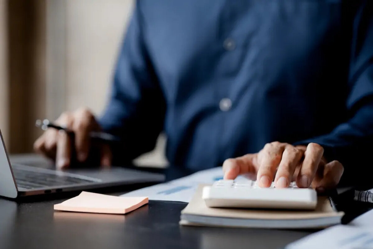 Businessman at desk using laptop with one hand and calculator with the other