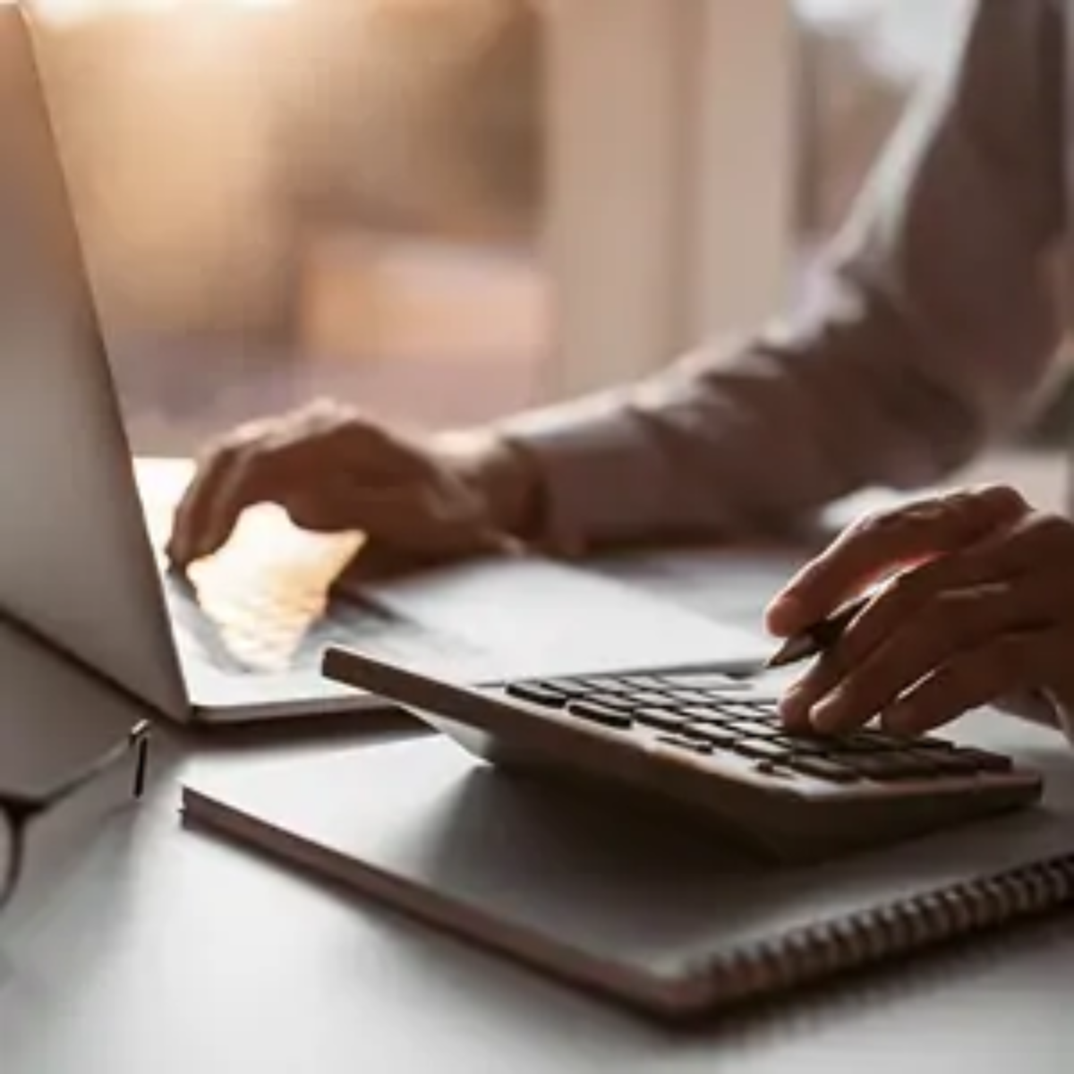 Businessperson at desk using laptop with one hand and calculator with other