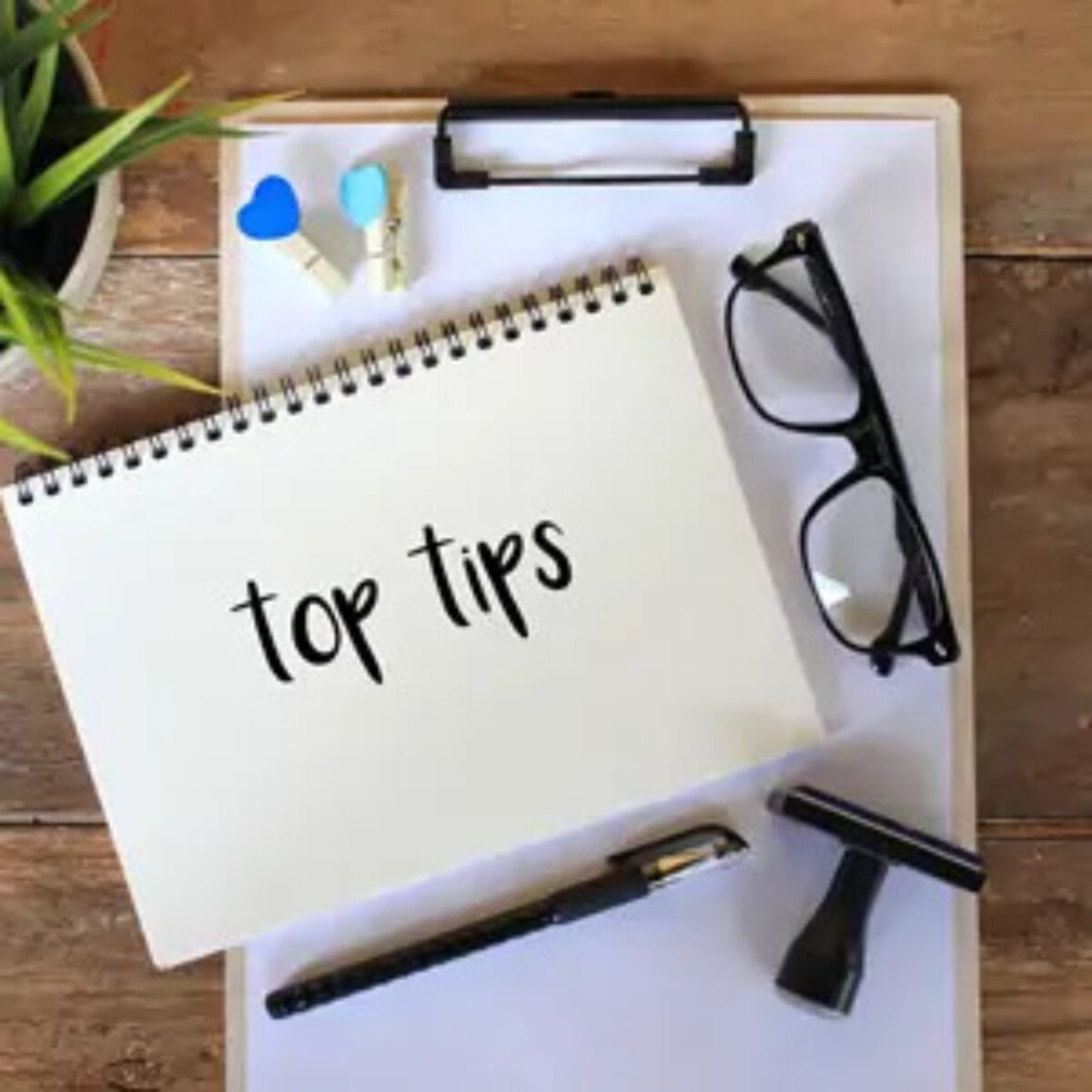 Open notebook with 'top tips' written on page on top of clipboard on desk