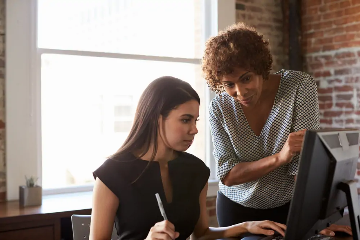 Businesswoman helping apprentice working on computer at desk