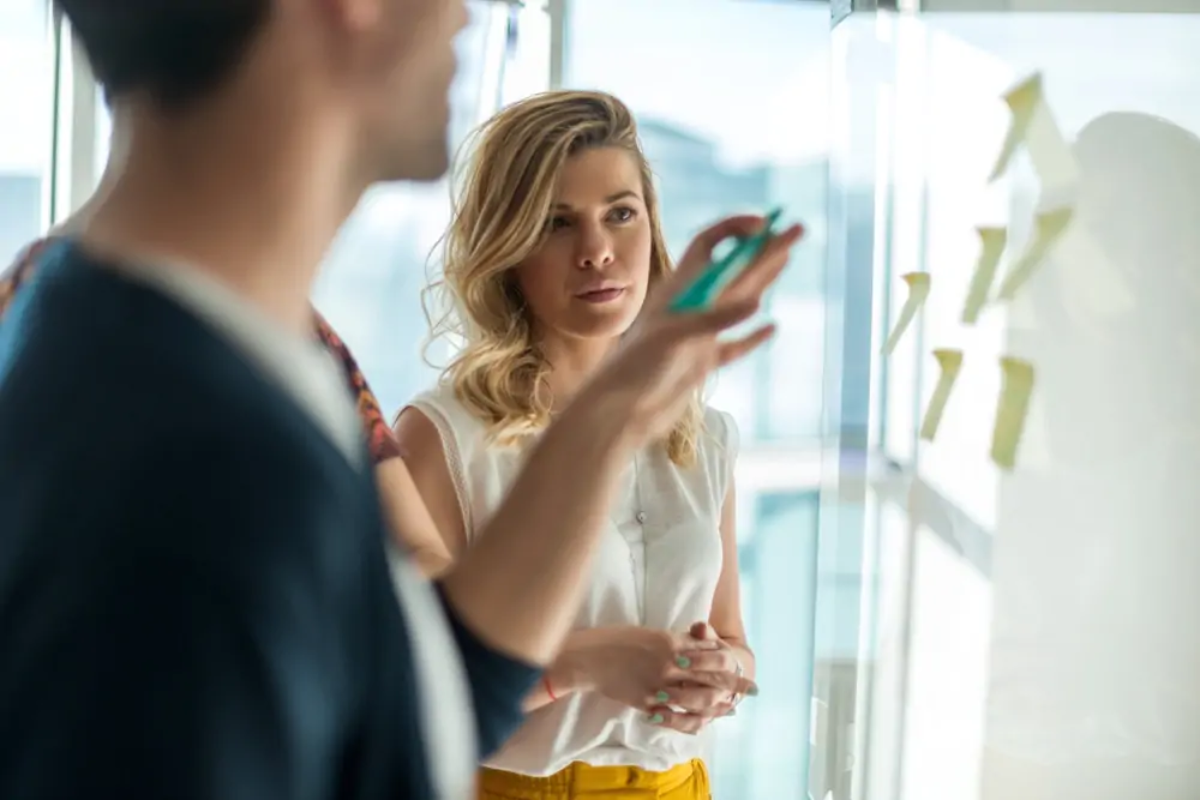 Businesspeople discussing post-it notes on whiteboard
