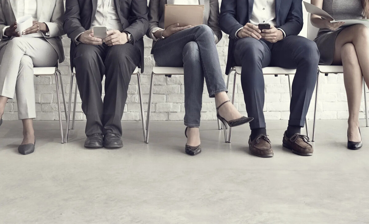 Bottom half of five interview candidates sitting on chairs in a row