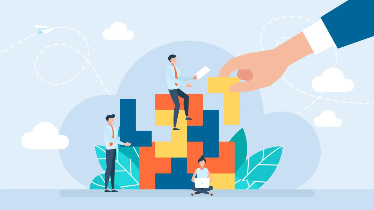 Cartoon of hand placing piece into Tetris-style puzzle with miniature businesspeople sitting and standing around puzzle with a laptop and document