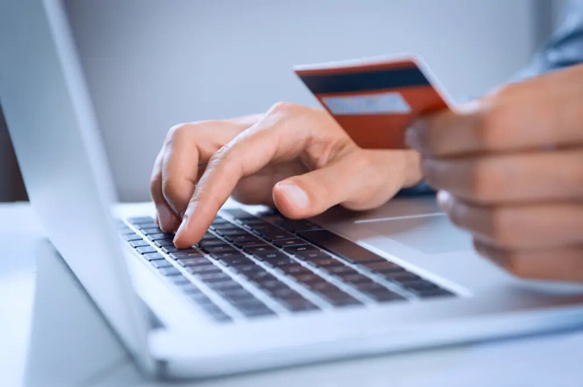 Man typing on laptop keyboard holding bankcard near