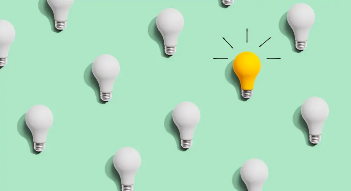 Cartoon of lightbulbs arranged in linear pattern, all switched off apart from one that is yellow with glow lines drawn around it