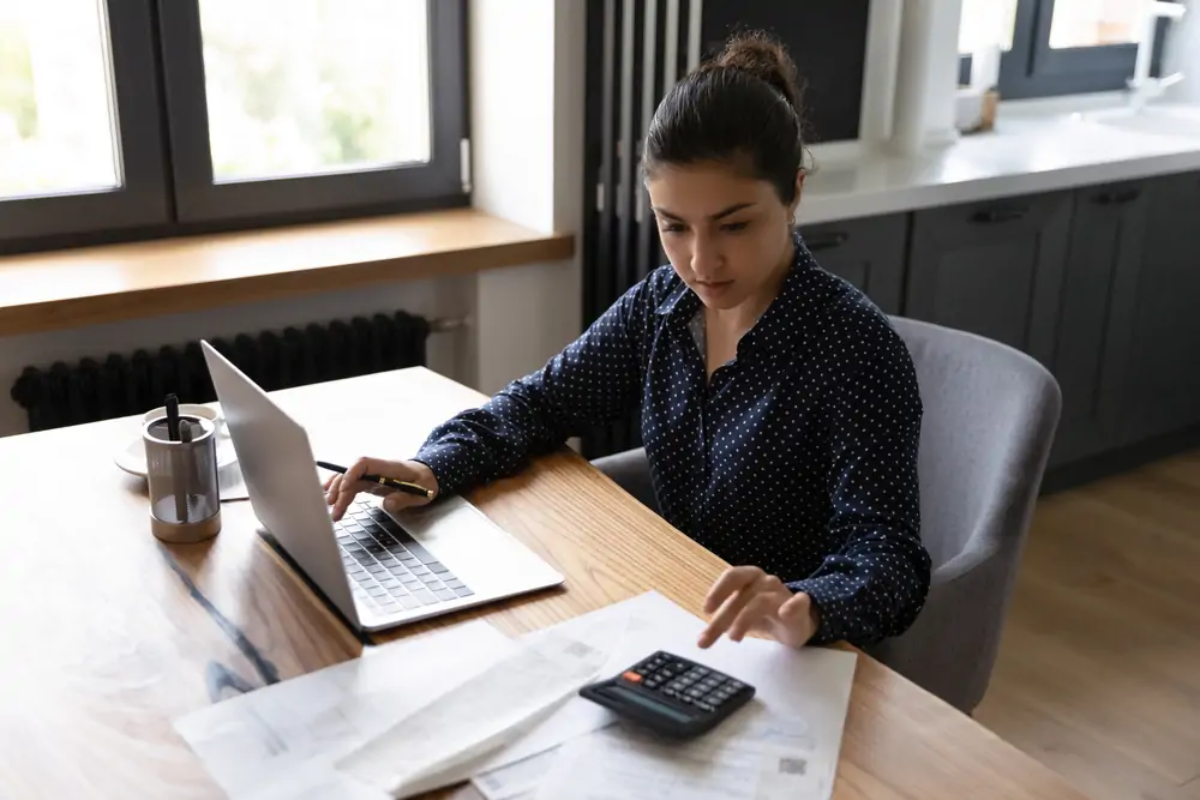 Businesswoman using calculator with one hand and laptop with the other to deal with late payments