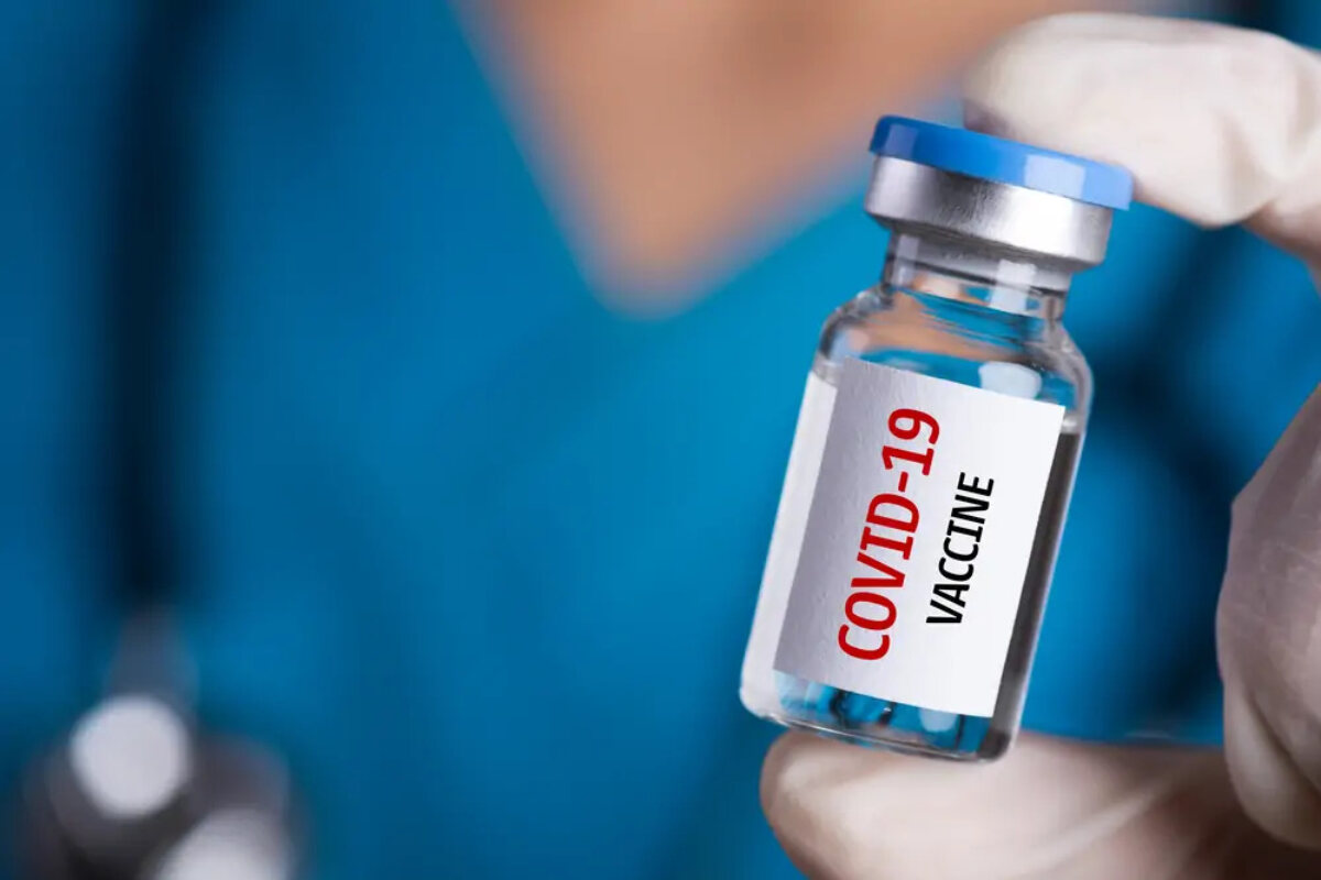 Medically gloved hand holding vial labelled 'Covid-19 vaccine'