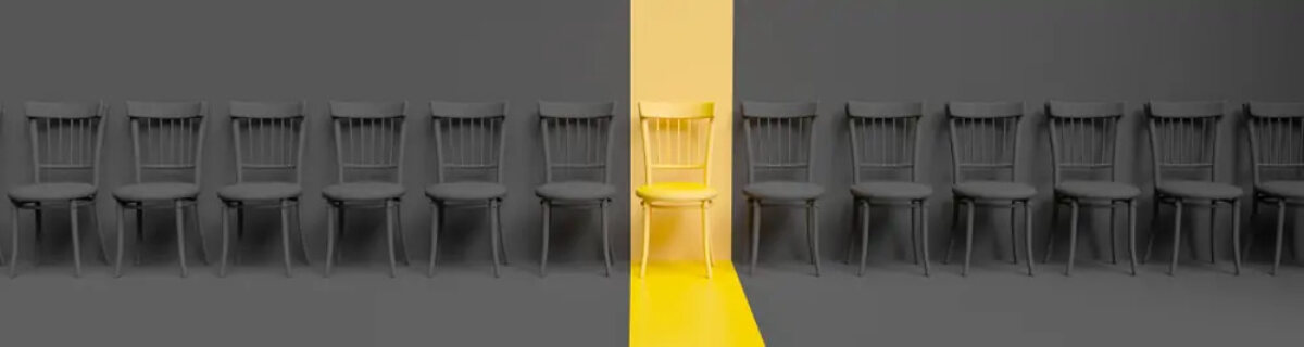 Row of chairs in dull grey lighting with a chair in the middle lit up with gold lighting