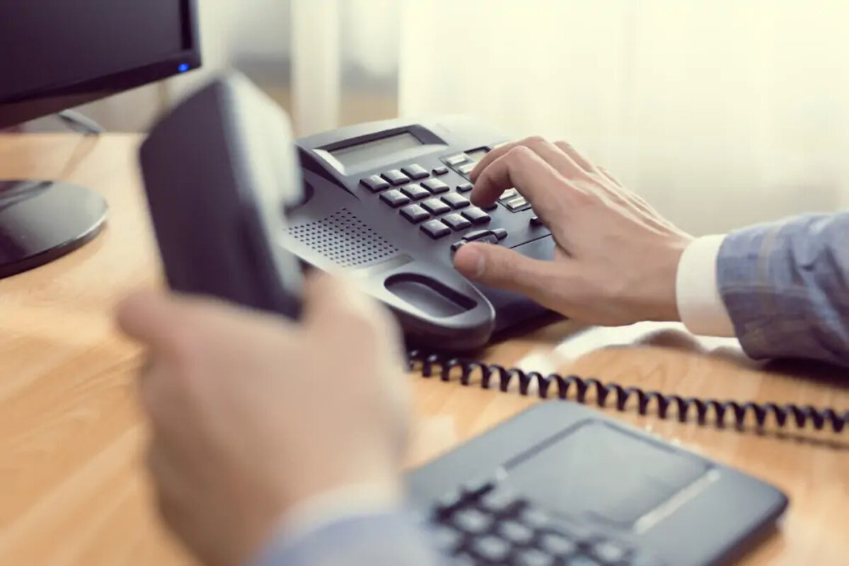 Businessman at desk holding phone receiver and dialing number in keypad