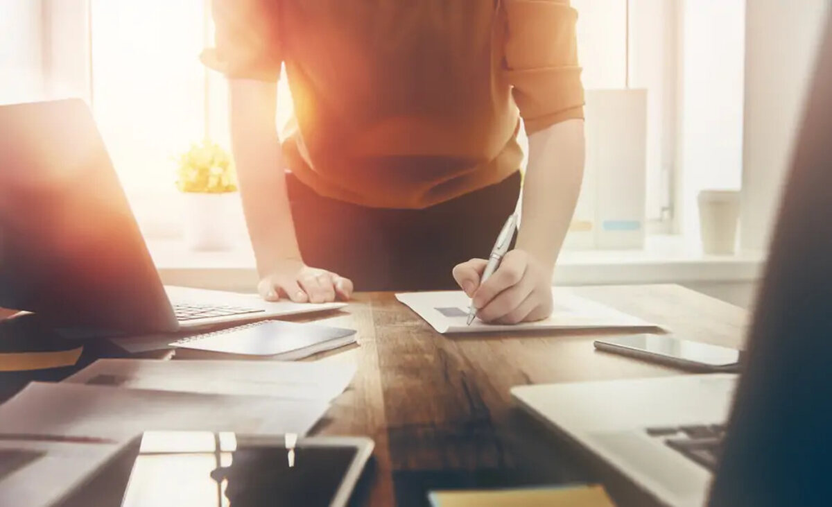 Business woman standing while writing on a document on desk next to laptop