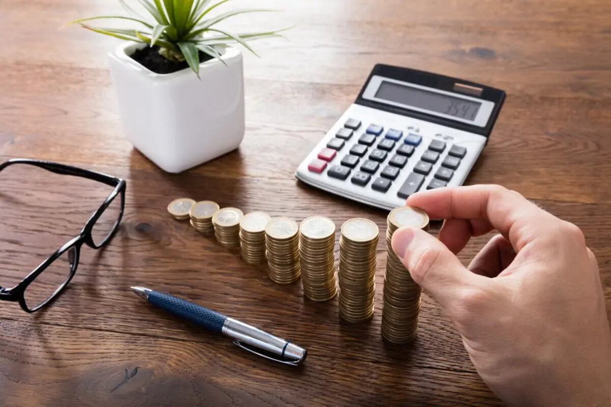 Hand making increasingly tall stacks of coins in front of calculator