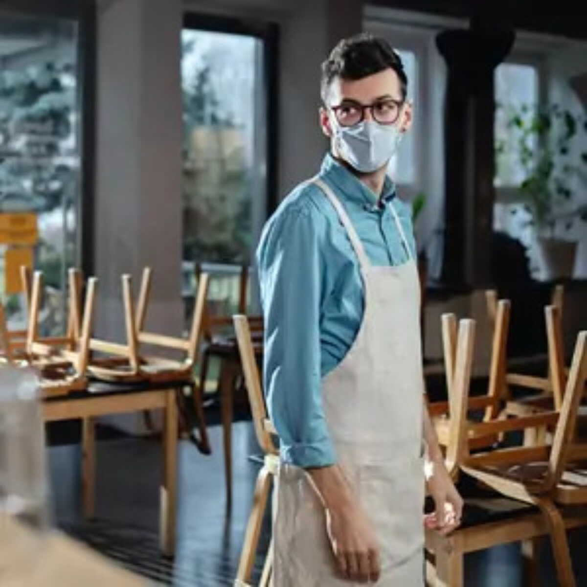 Waiter wearing facemask standing in closed restaurant