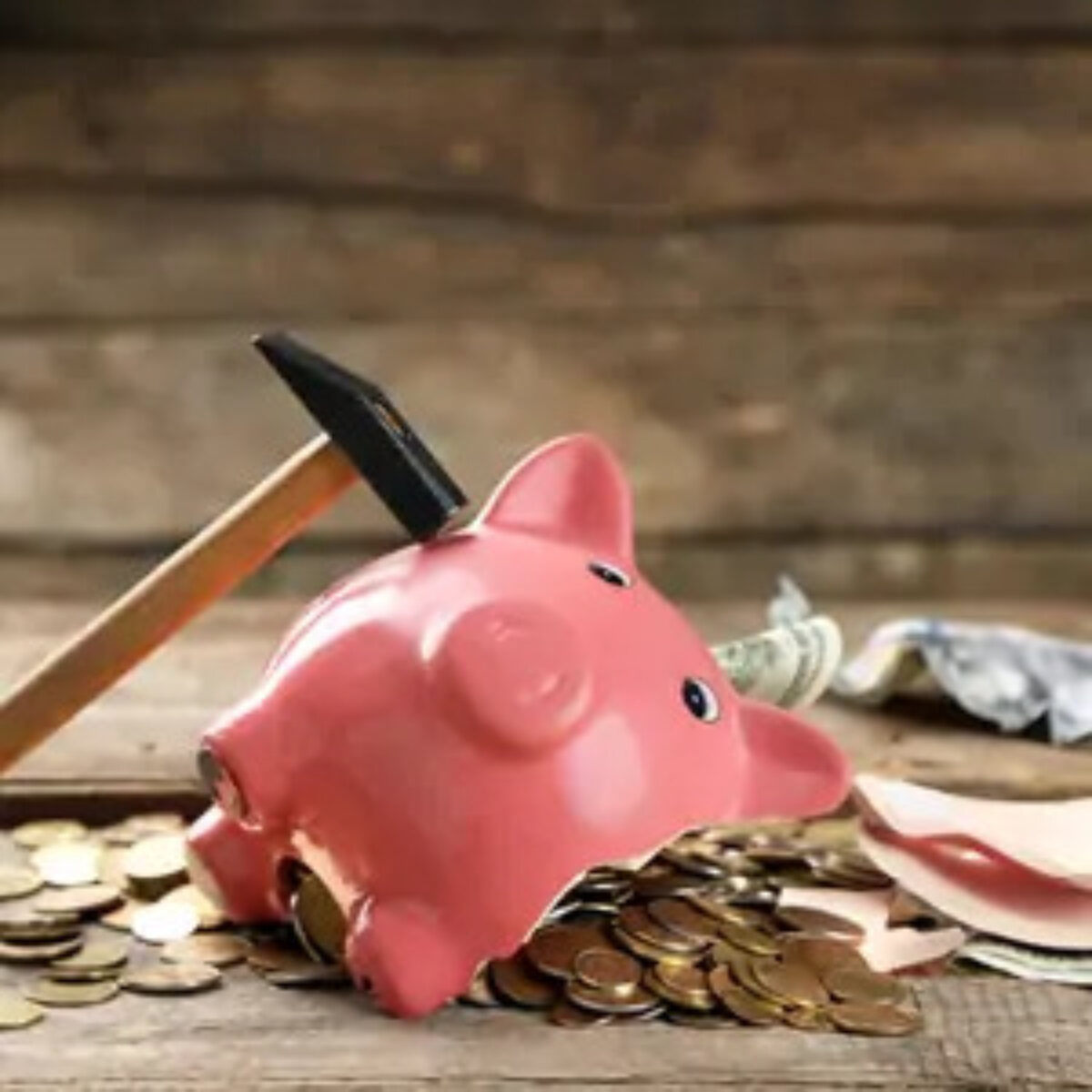 Broken piggy bank on ground with coins spilling out of side and a hammer resting on the other side