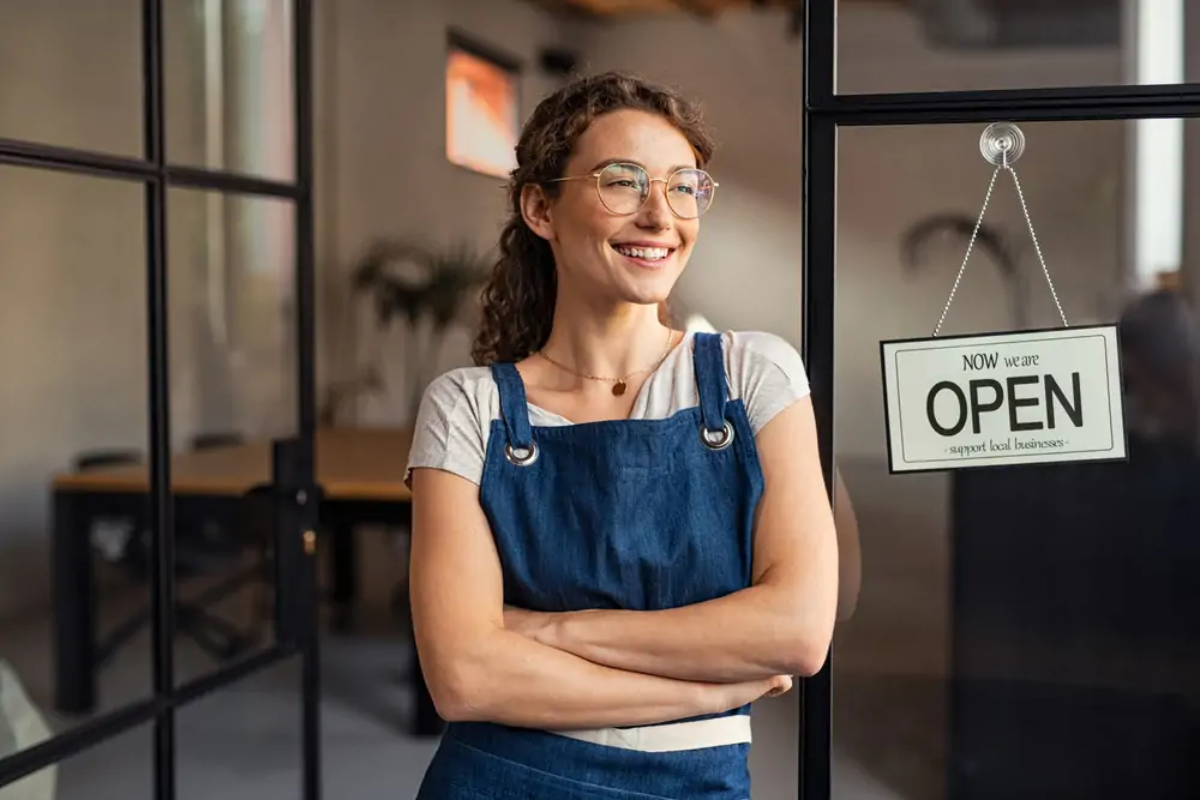 Hospitality business owner standing smiling by door with 'open' sign on it