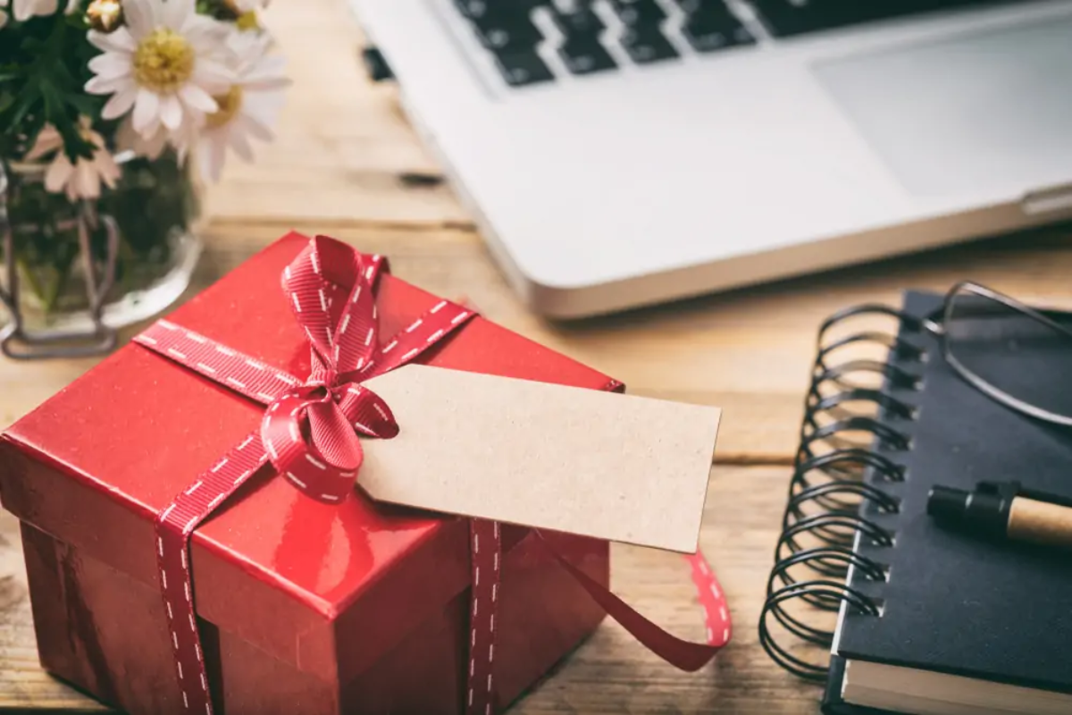 Small Christmas gift on wooden desk next to notebook and laptop